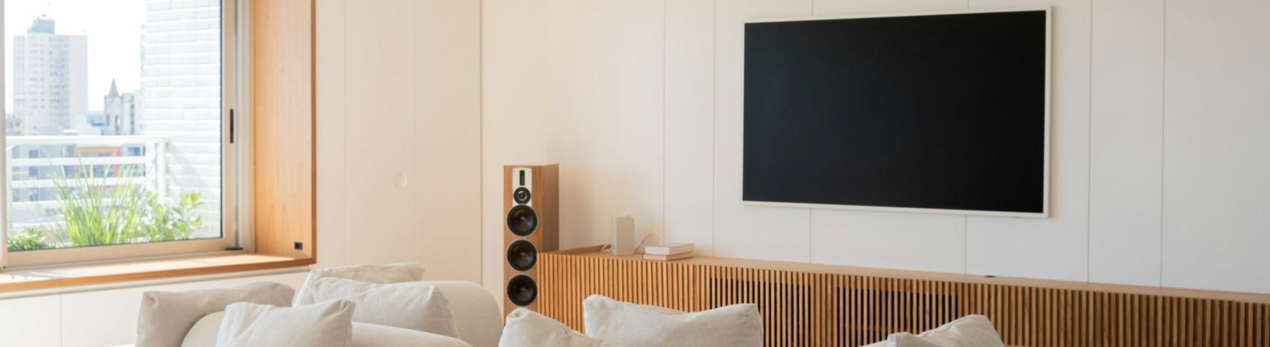 Bright living room with a large sectional sofa, wall-mounted TV and a floor-standing speaker