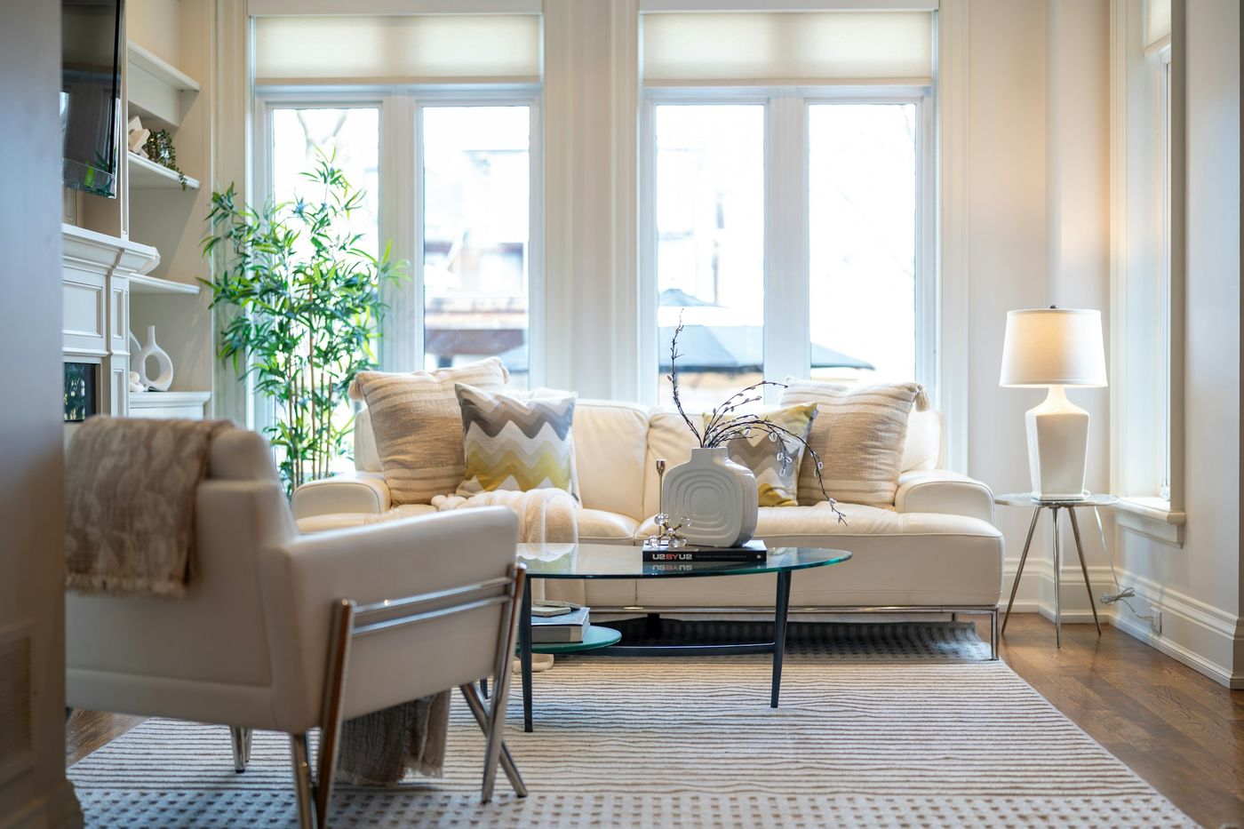 Sunlit living room with shades on tall bay windows and light-colored sofas