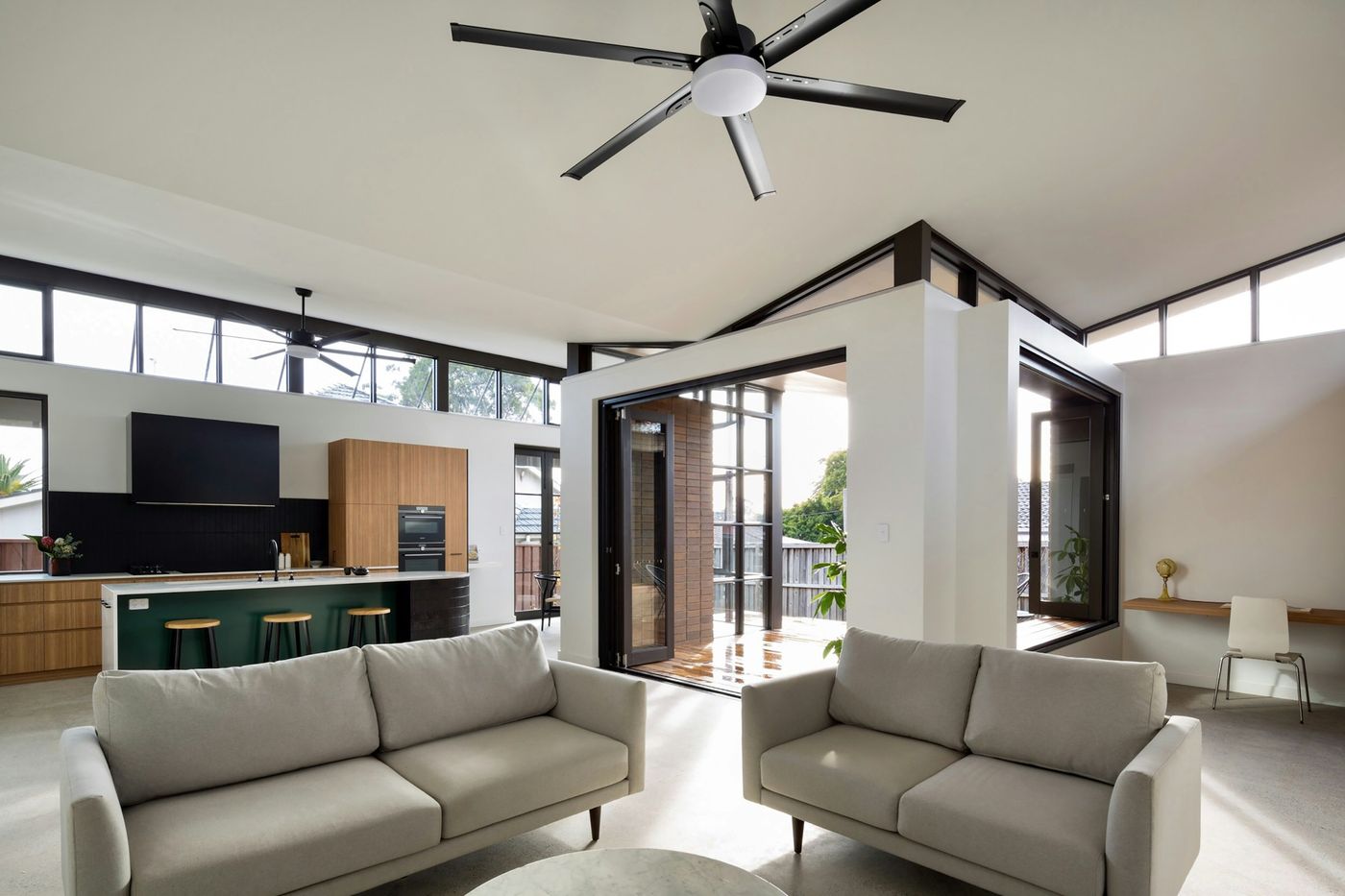 Open modern living room with a black ceiling fan, grey sofas and large clerestory windows