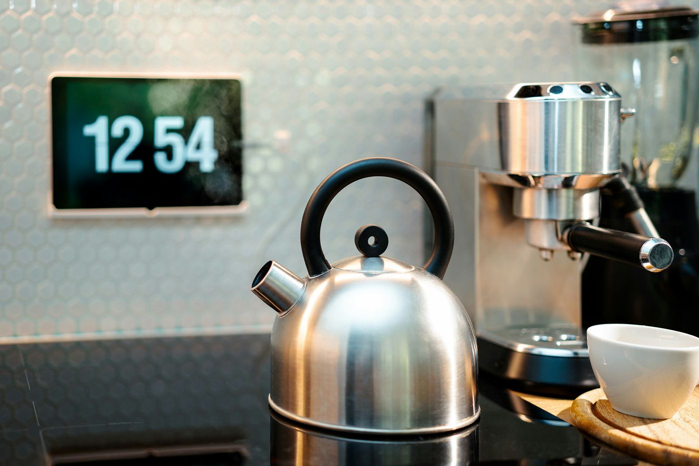 Wall-mounted touch display showing the time above a kitchen counter with a kettle and coffee machine