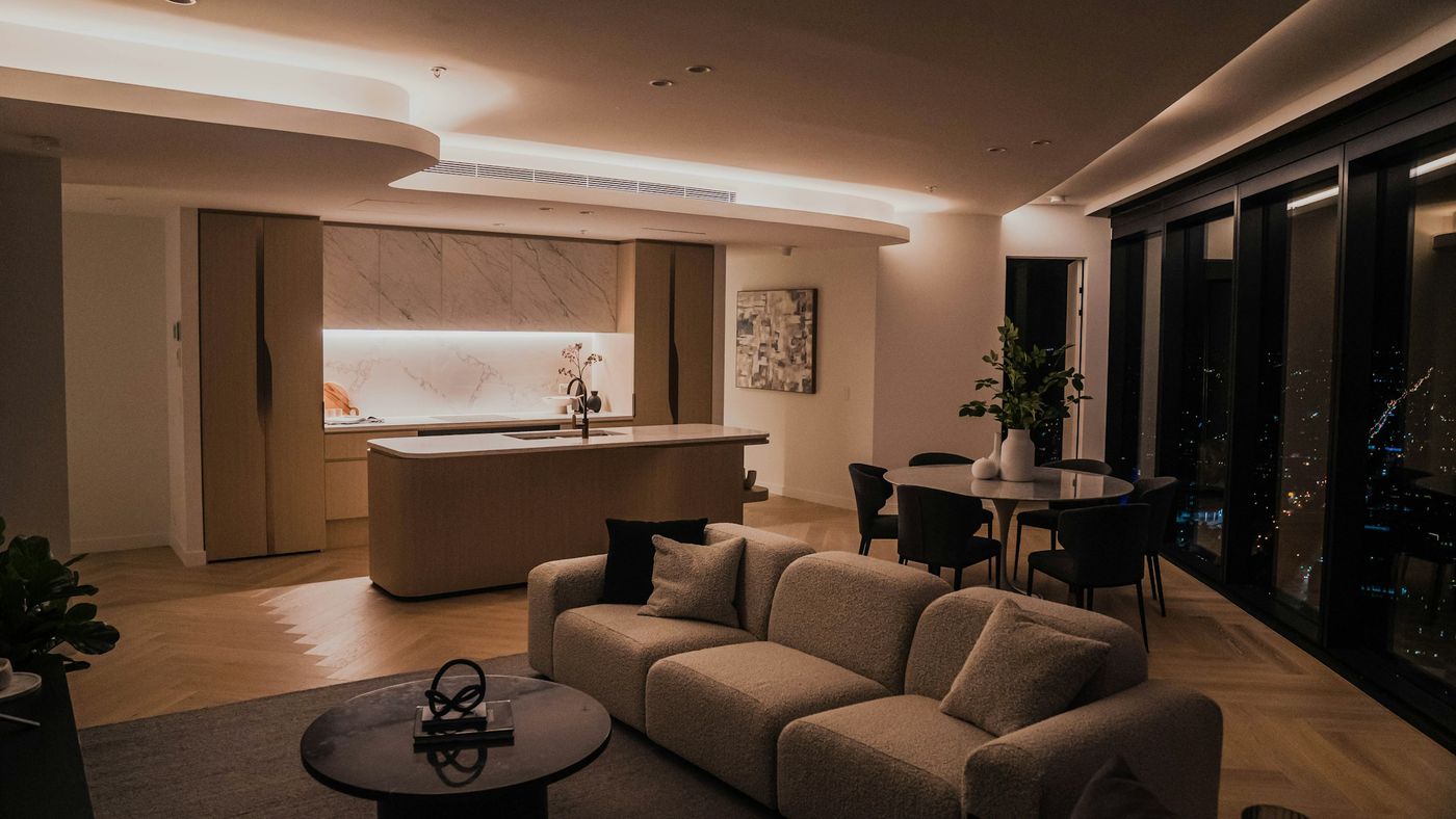 Modern living room in the evening with warm cove lighting, a sofa and a dining area