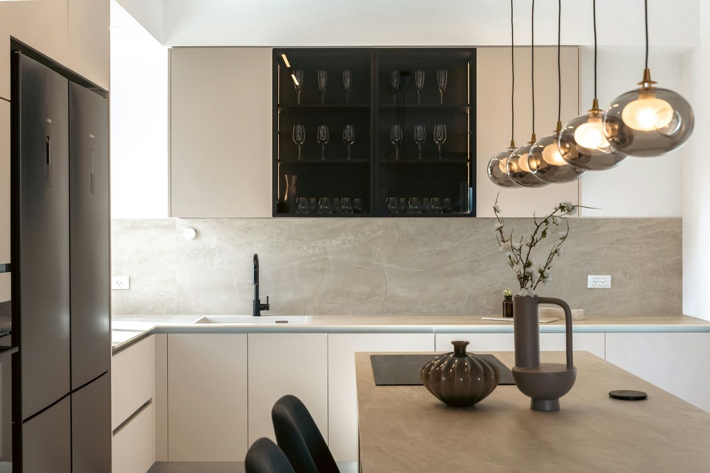 Modern kitchen with a row of glass pendant lights over the island and a lit glass cabinet