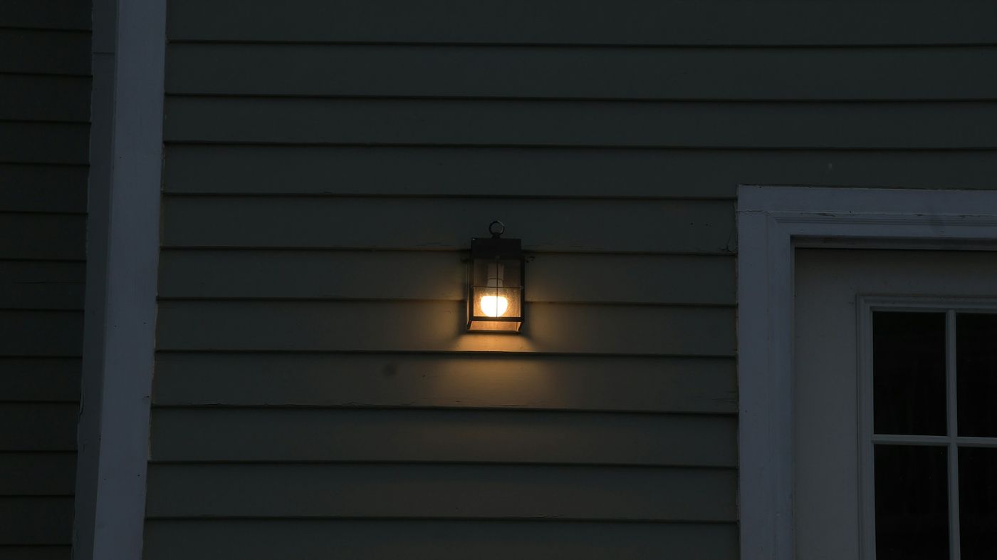 Wall lantern glowing on dark exterior siding at night
