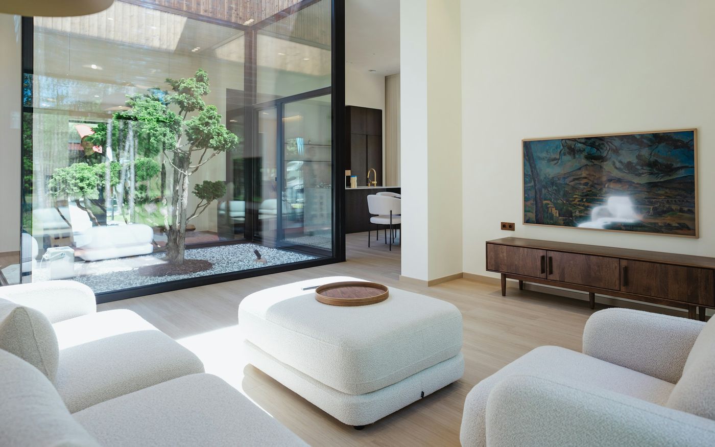 Bright living room with a large wall-mounted TV, white sofas and a glass wall to a courtyard