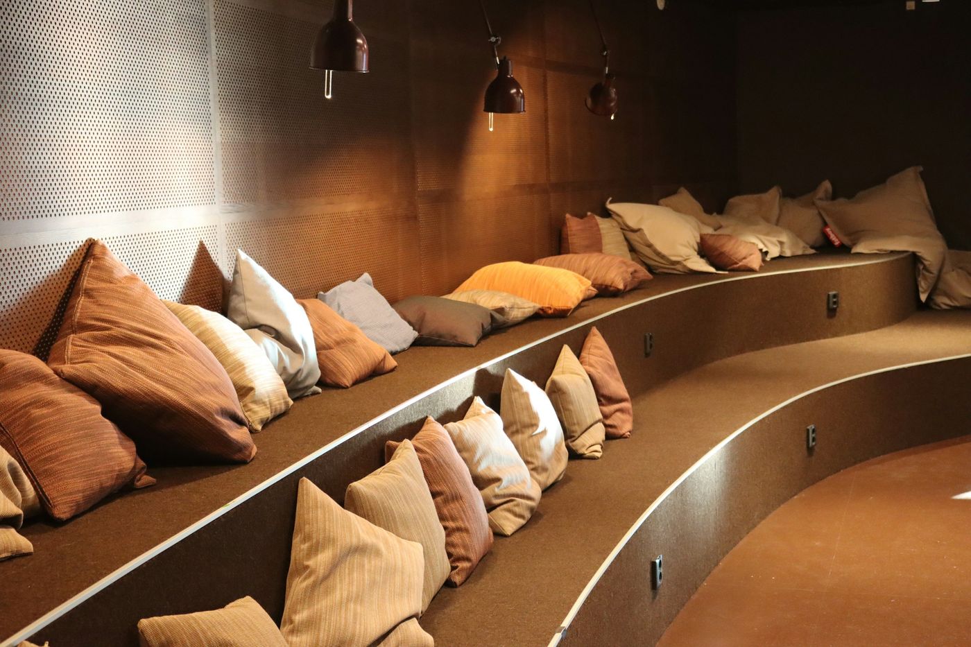 Curved tiered bench seating with cushions and warm pendant lights