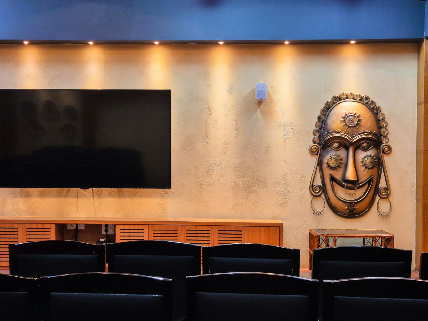 Media room with downlights washing a textured wall, a wall-mounted TV, sculptural art and dark seating