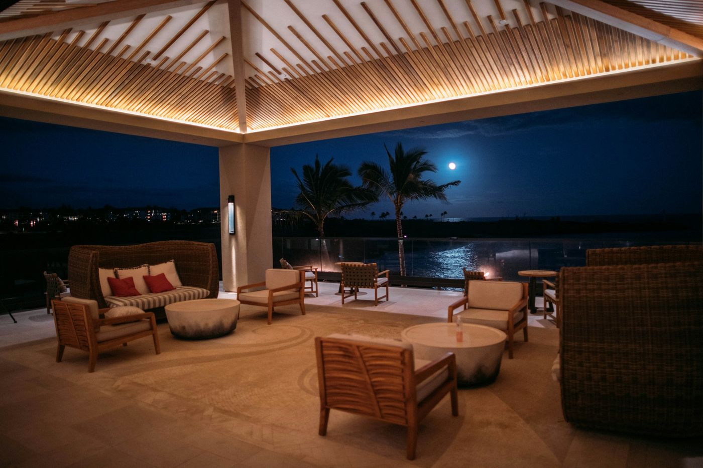 Covered outdoor living area with lounge furniture overlooking the water at night