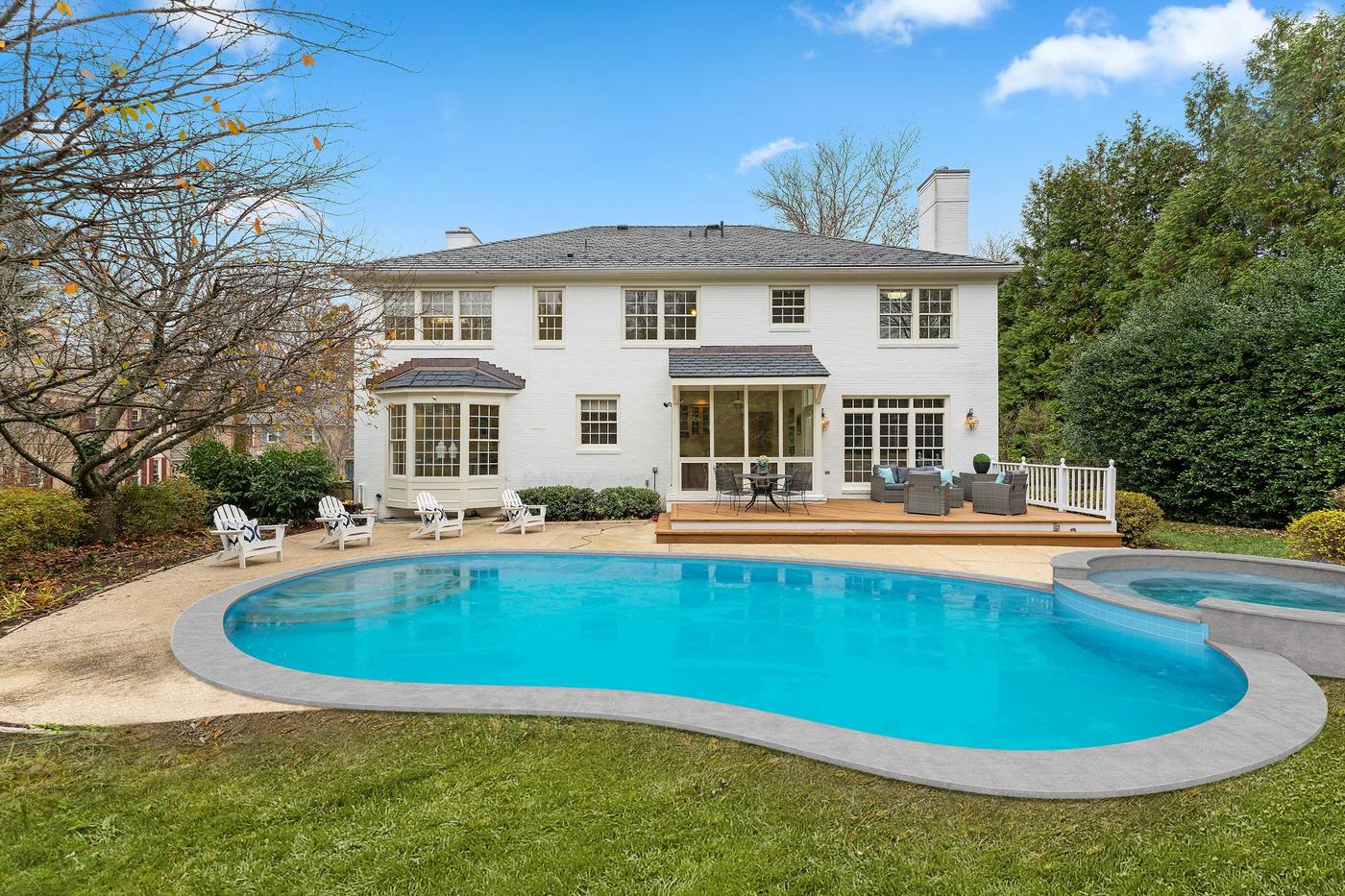 Backyard with a curved swimming pool and attached spa behind a large white house