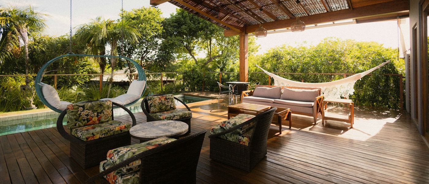 Covered patio with lounge seating and a hammock under a slatted pergola, overlooking a garden