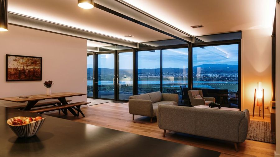 Open living room at dusk with linear cove lighting along the ceiling and a wall of windows