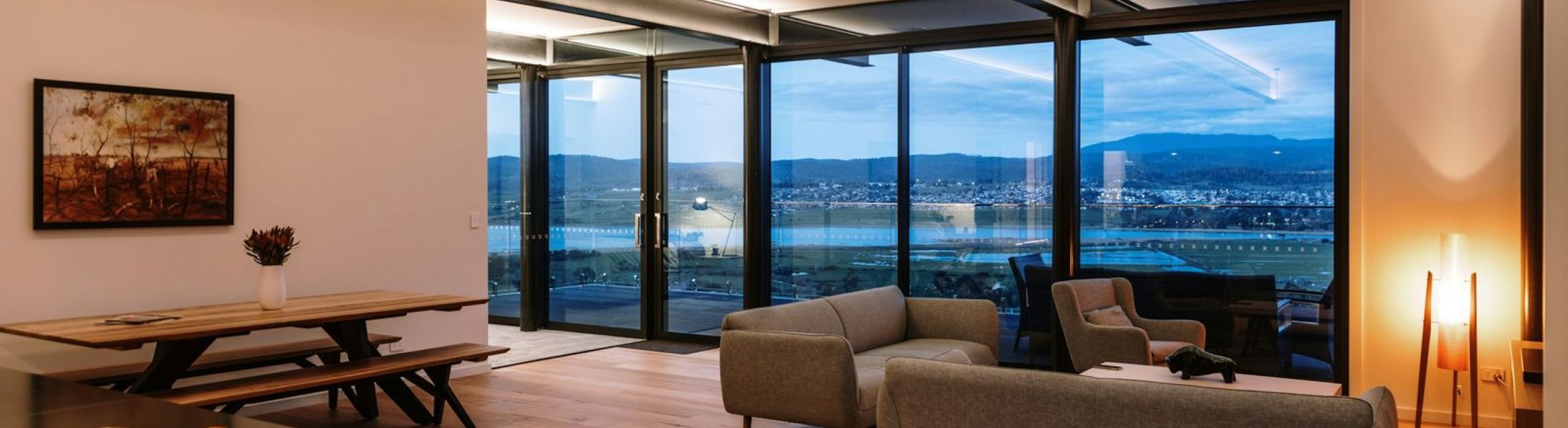 Open living room at dusk with linear cove lighting along the ceiling and a wall of windows
