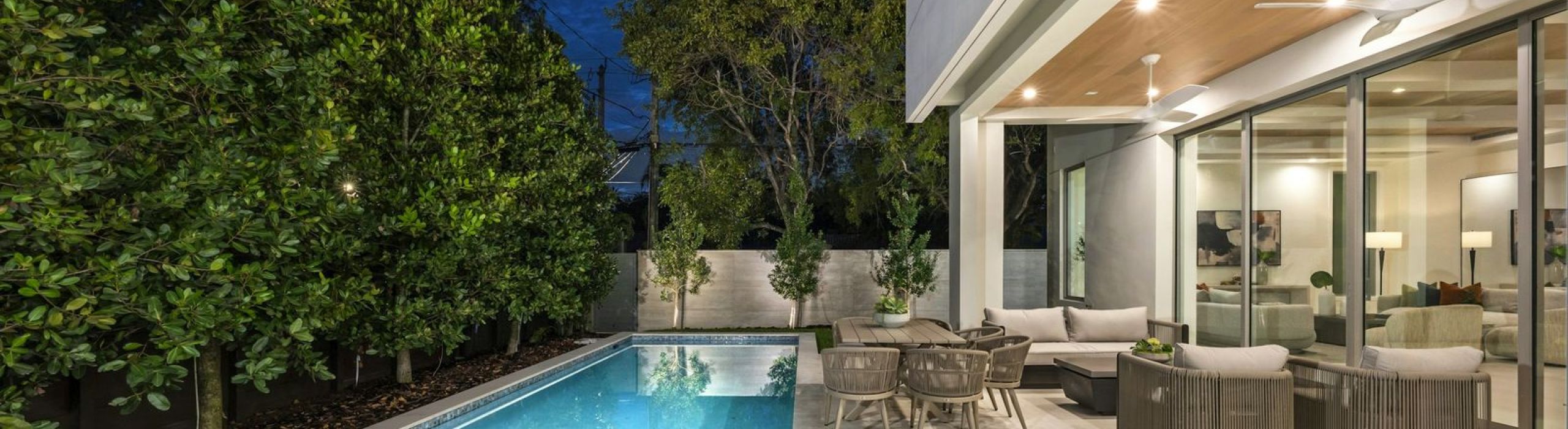 Modern home at dusk with a lit lap pool and a covered outdoor lounge